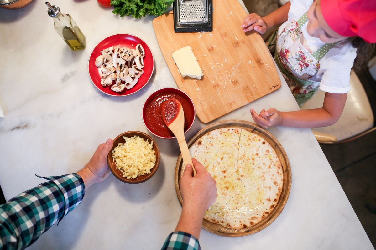 Father topping a ready-made pizza base on a wooden board at home